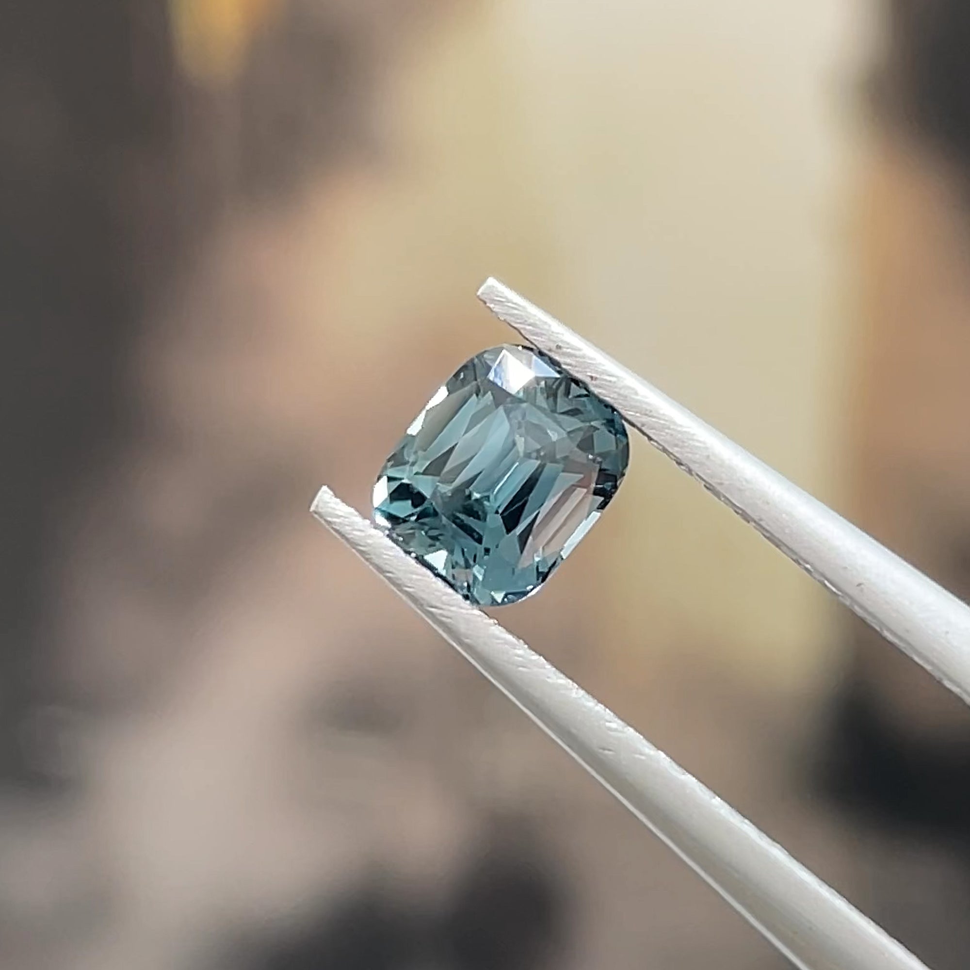 Precision Cut 0.78 ct Teal Spinel from Mahenge Tanzania, tweezer view, beige background