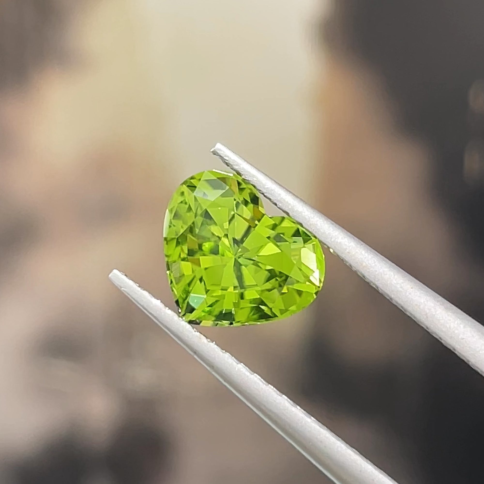 2.01 carat Precision Cut Heart shape peridot from Pakistan, tweezers view, beige background