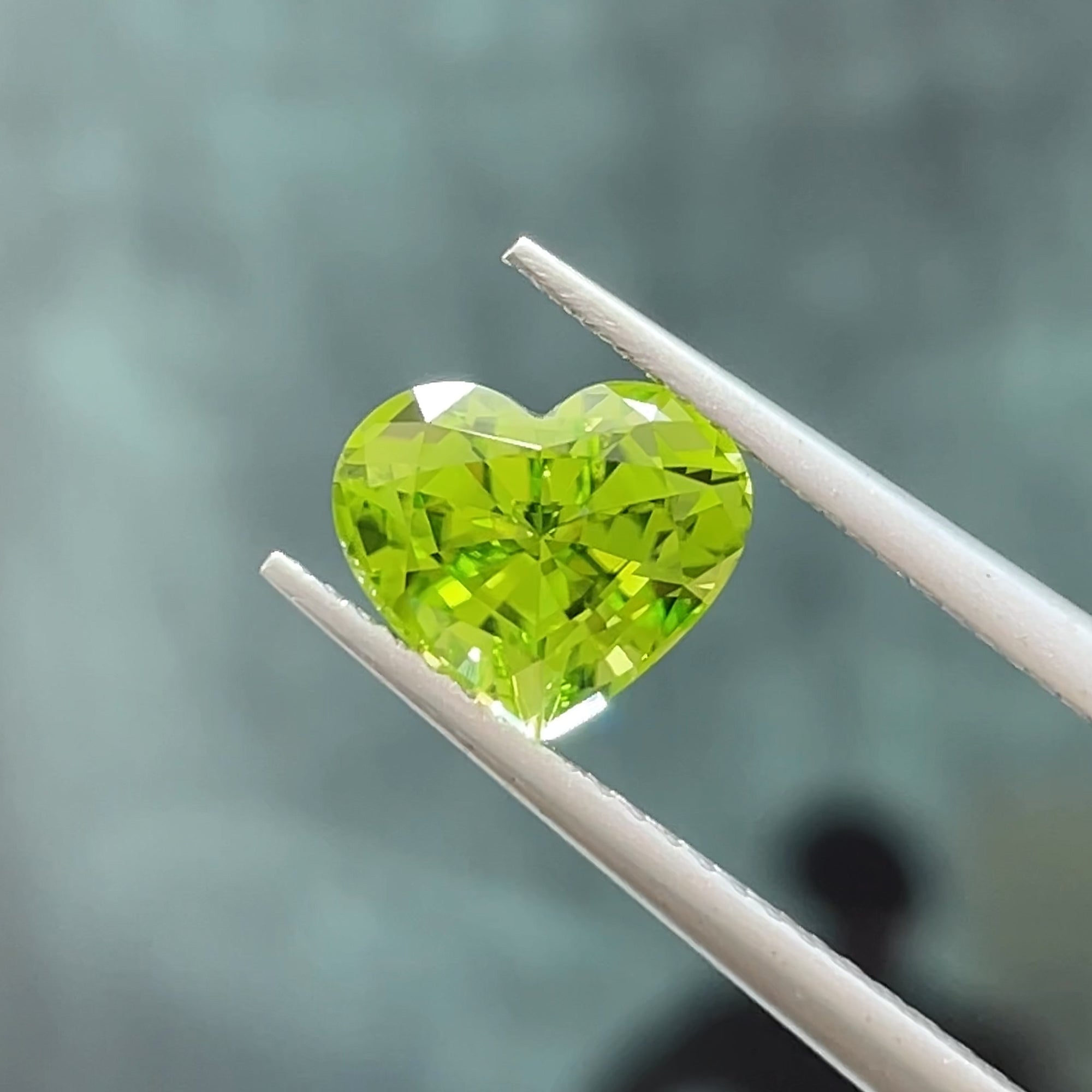 2.01 carat Precision Cut Heart shape peridot from Pakistan, tweezers view, light navy background