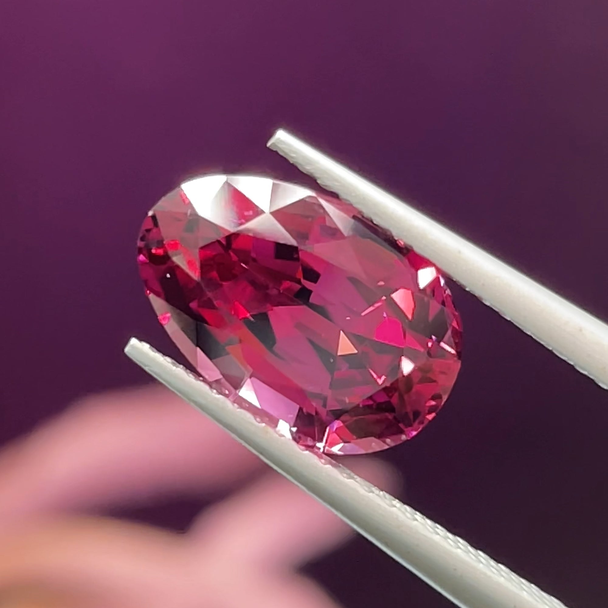 4 carat Precision Cut umbalite Garnet from tanzania, egg shape, tweezers view, purple background