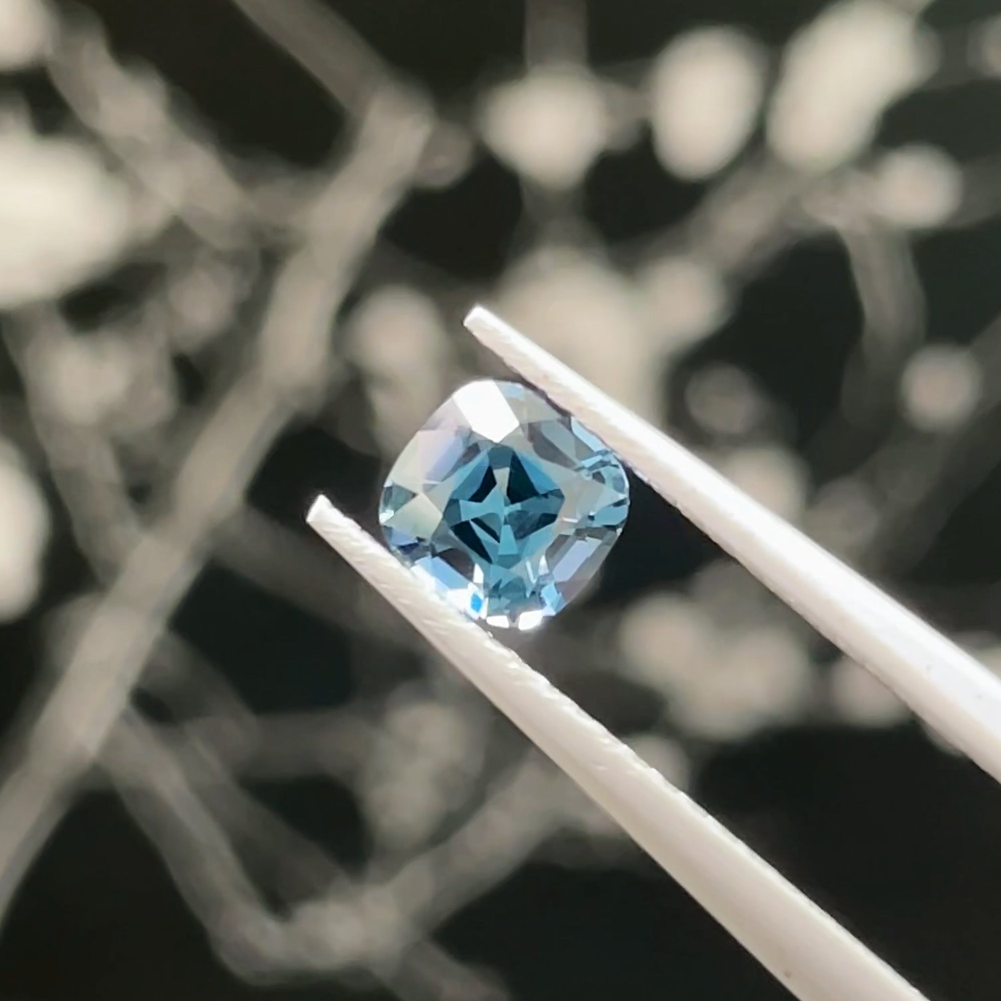 0.70 ct Precision Cut Teal Spinel, tweezers view, black background