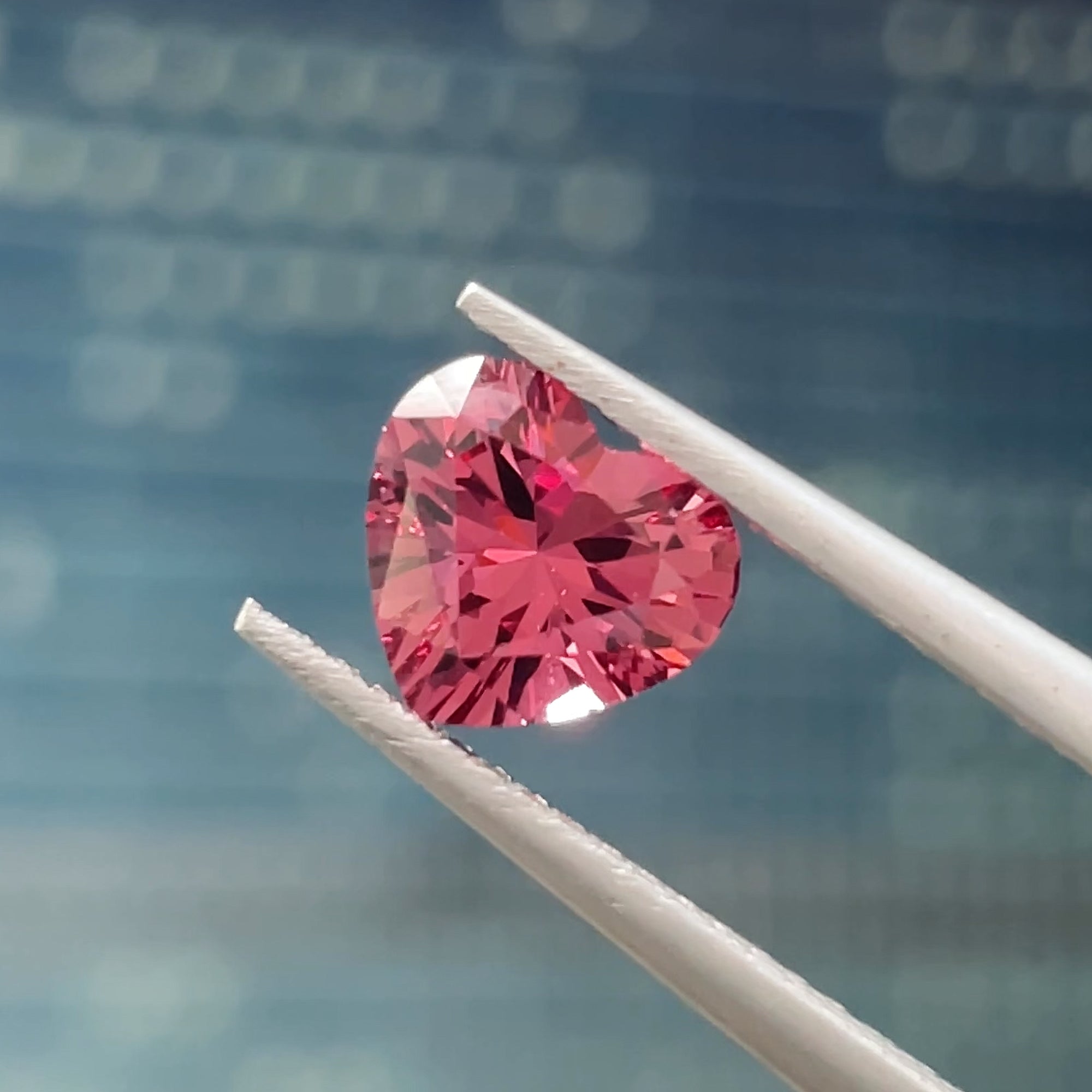 1.32 ct Purplish Pink Malaya Garnet from Tanzania, precision cut, tweezers view, blue background