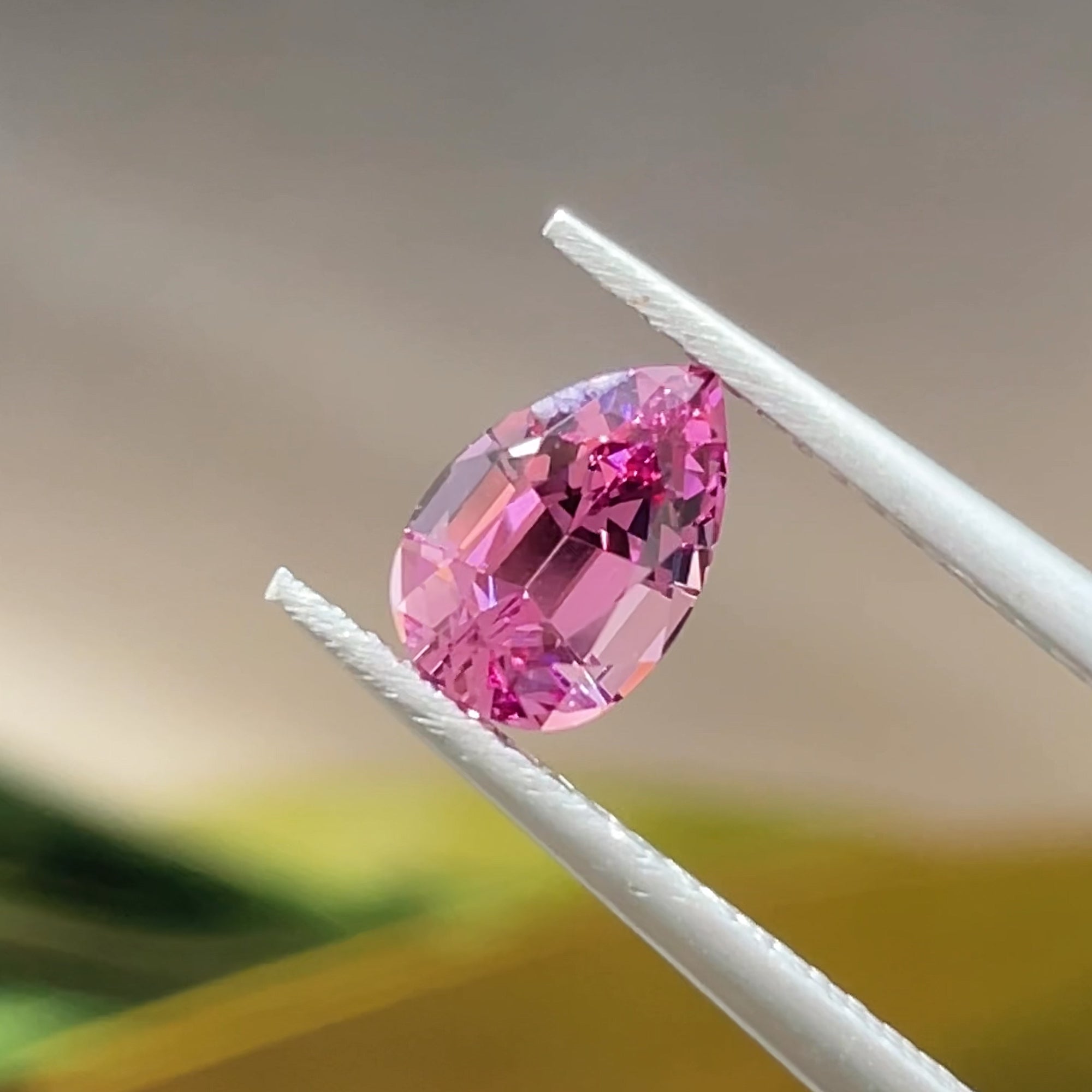 1.27 ct Magenta-Pink Lindi garnet from Tanzania, precision cut, tweezers view, beige background