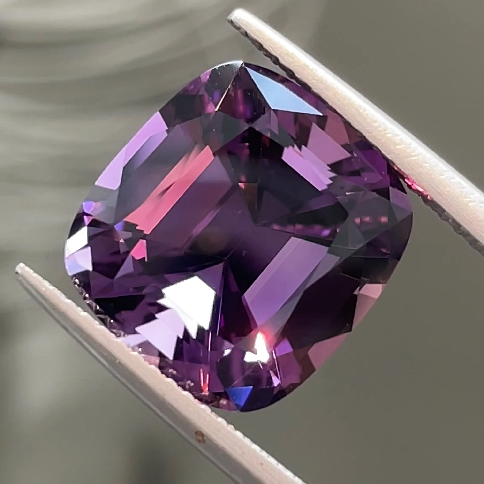 Precision cut 8.12 ct Rwandan Amethyst, tweezers view, grey background