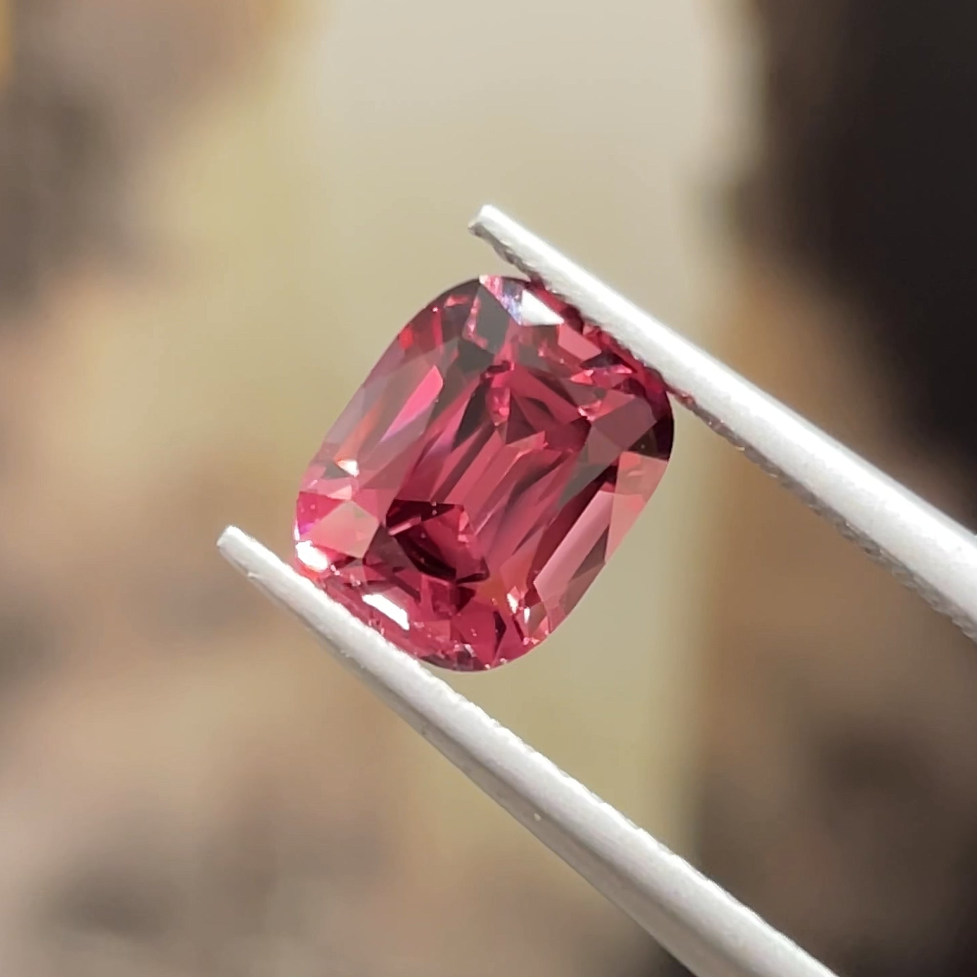 1.72 ct Malaya Garnet from Tanzania, precision cut, tweezers view, beige background