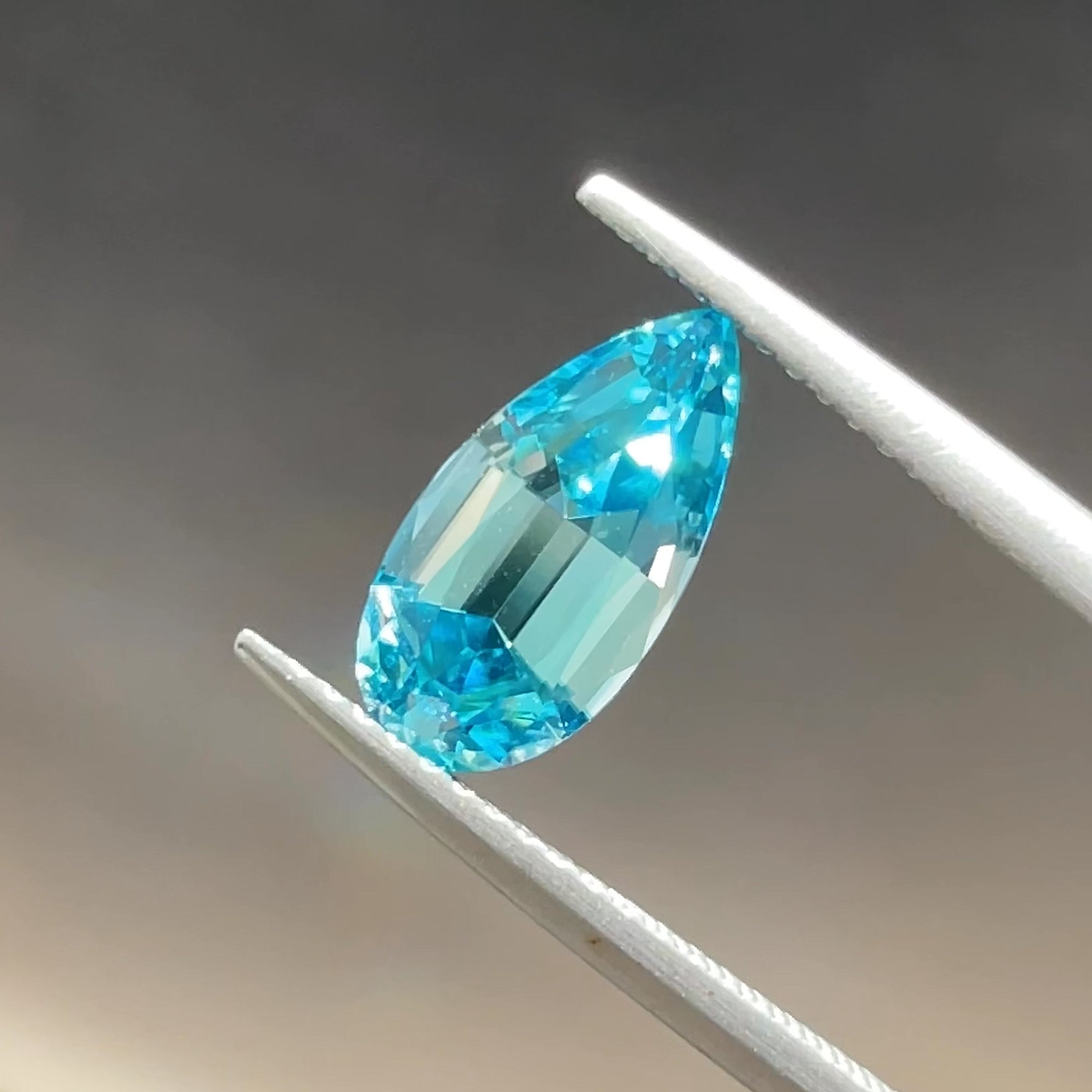 2.76 ct Blue Zircon from Cambodia, precision cut, tweezers view, grey background