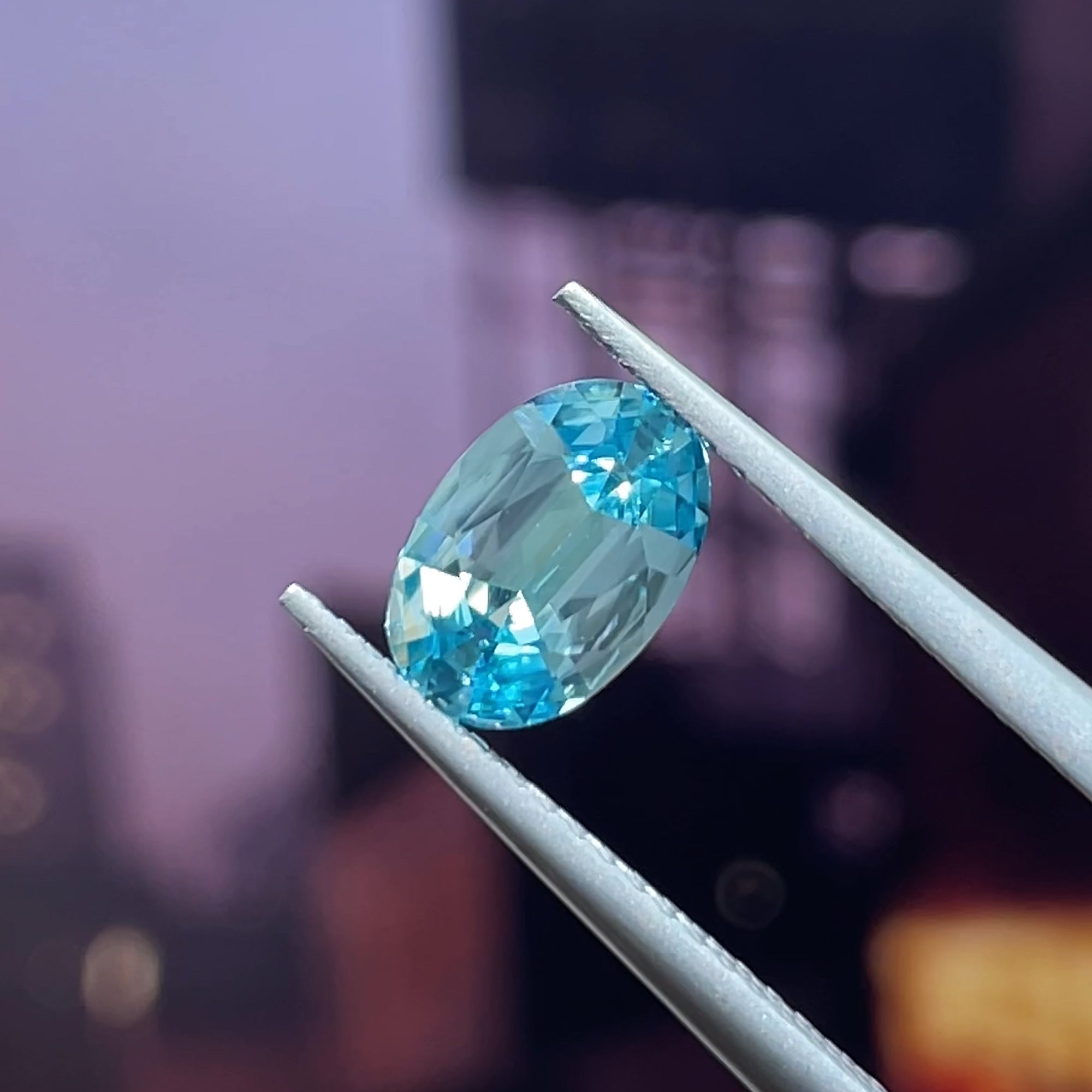 1.71 ct Cambodian Blue Zircon, precision cut oval, tweezers view, purple background