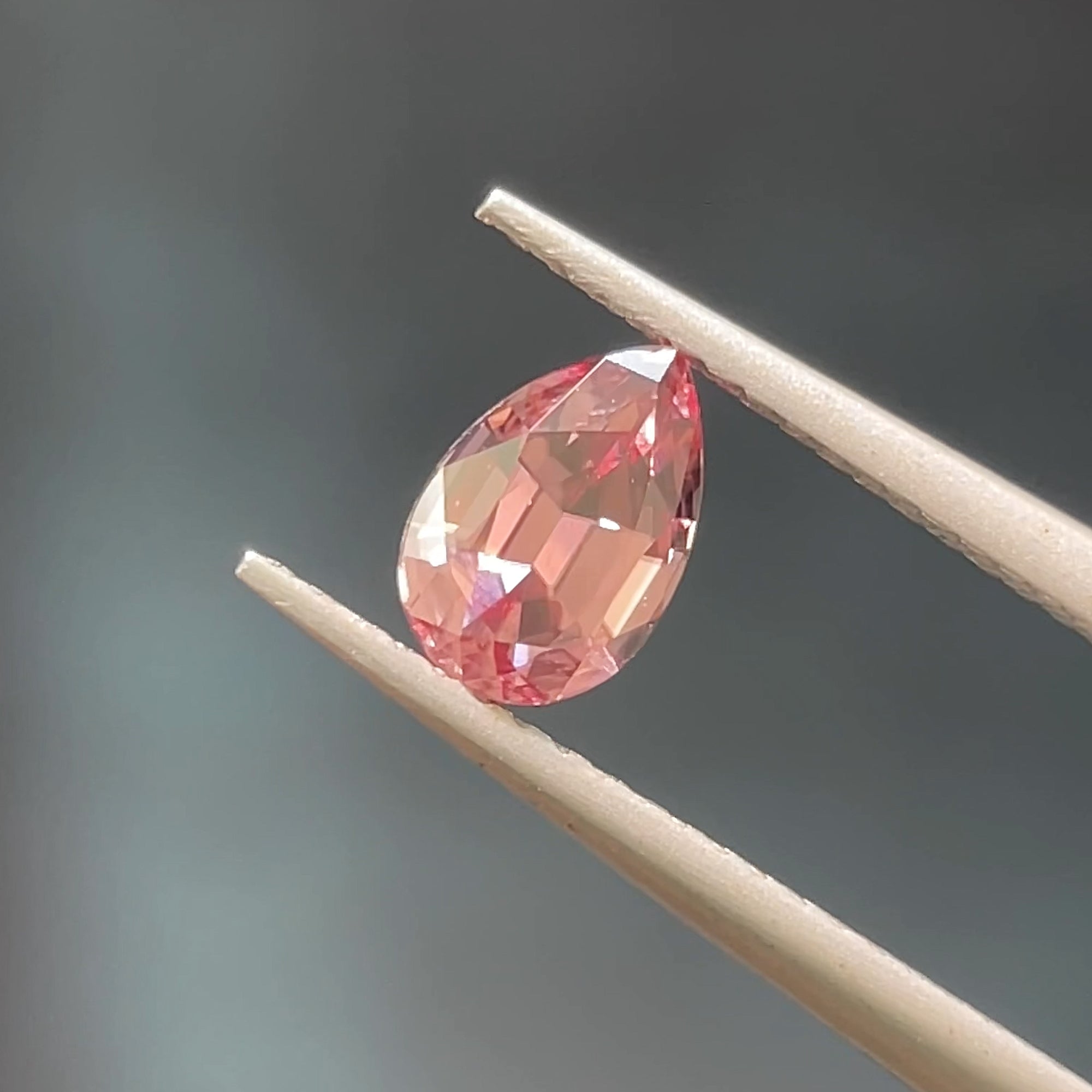 Unheated Pink Zircon from mozambique, precision pear shape, tweezers view, blue backgraound