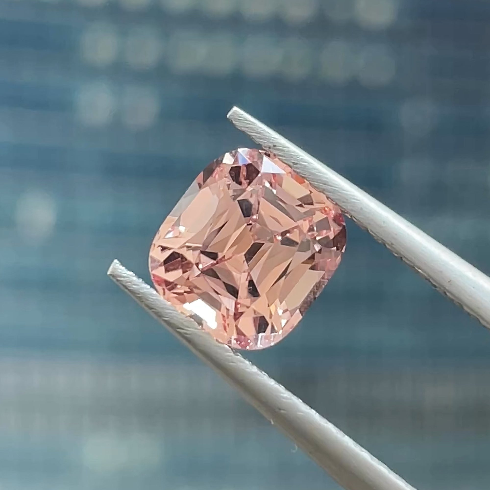 1.82 ct Precision cut Peachy-Pink Mahenge Garnet from Tanzania, cushion shape, tweezers view, black & blue background