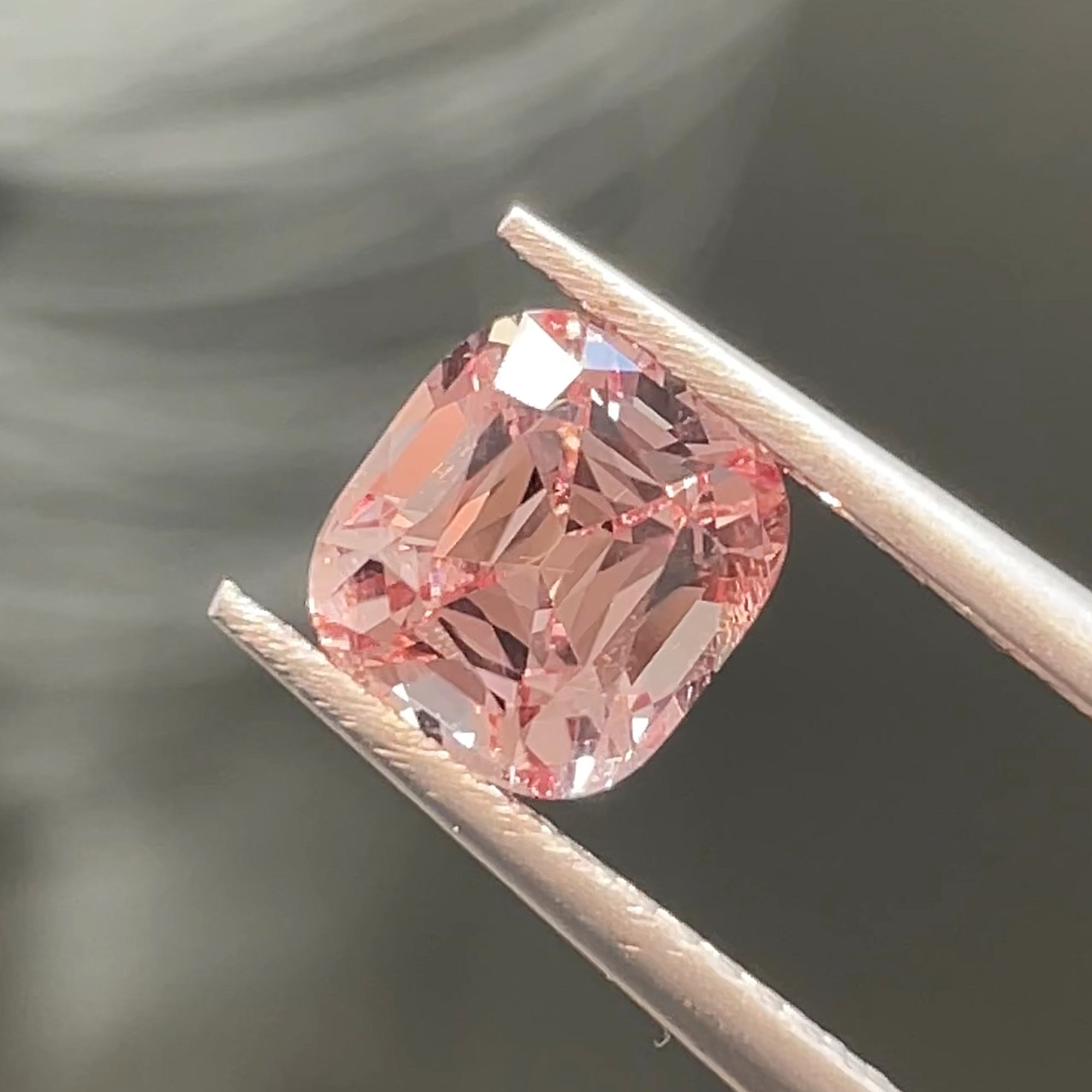 1.82 ct Precision cut Peachy-Pink Mahenge Garnet from Tanzania, cushion shape, tweezers view, direct light, neutral grey background