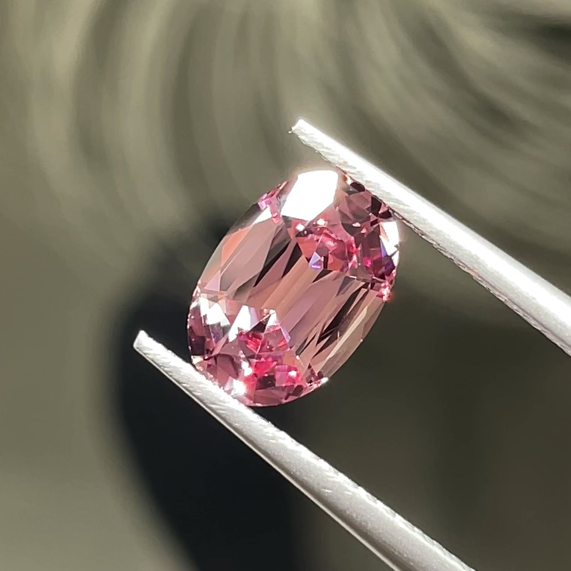 1.74 ct Precision Cut Rose Pink Mahenge Garnet from Tanzania, oval shape, tweezers view on neutral grey background