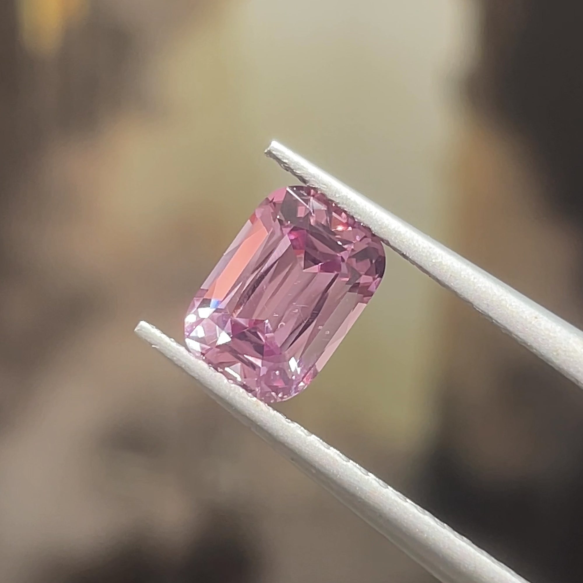1.39 ct Mauve Pink Mahenge Spinel, precision cut, tweezers view, diffuse light, beige background