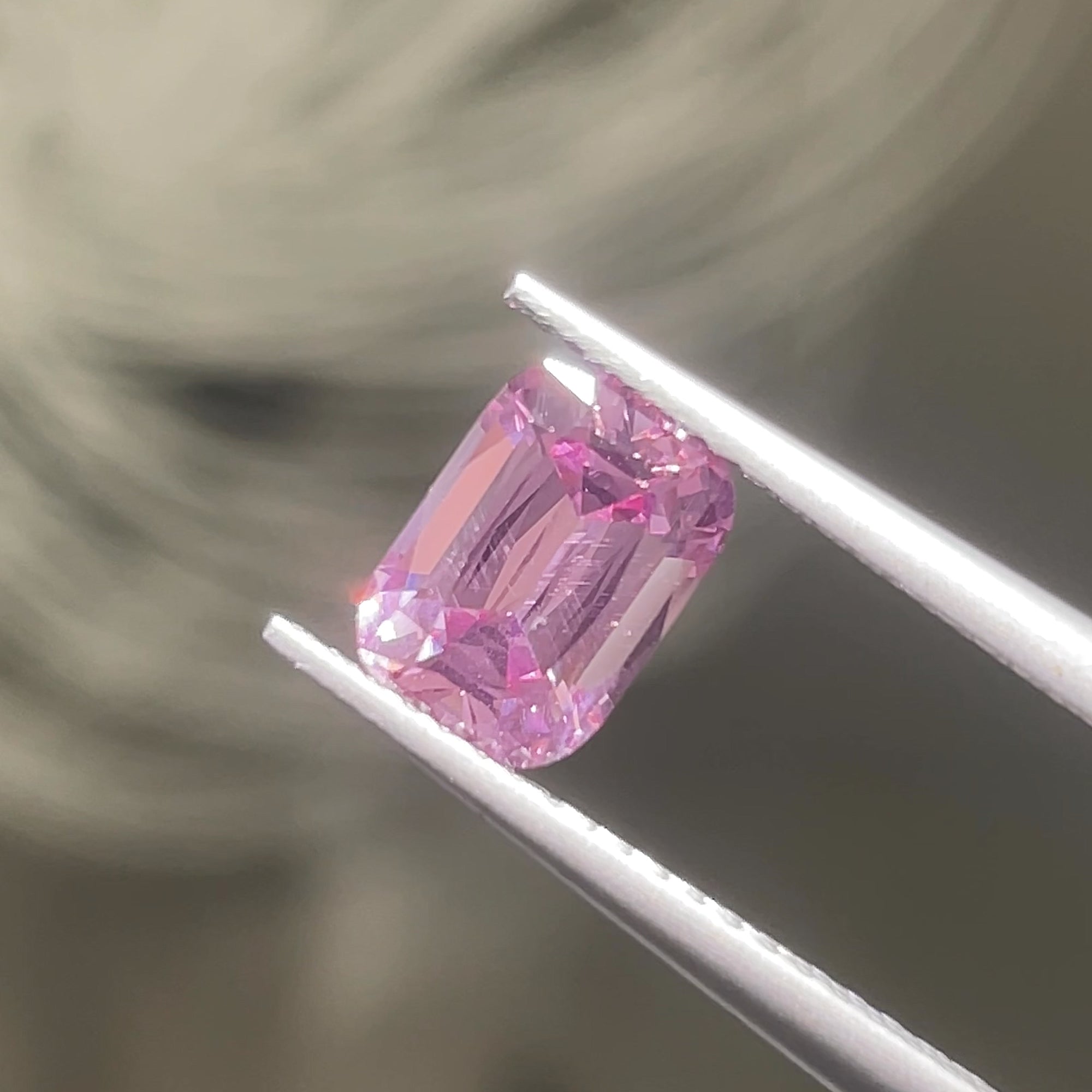 1.39 ct Mauve Pink Mahenge Spinel, precision cut, tweezers view, direct light, grey background