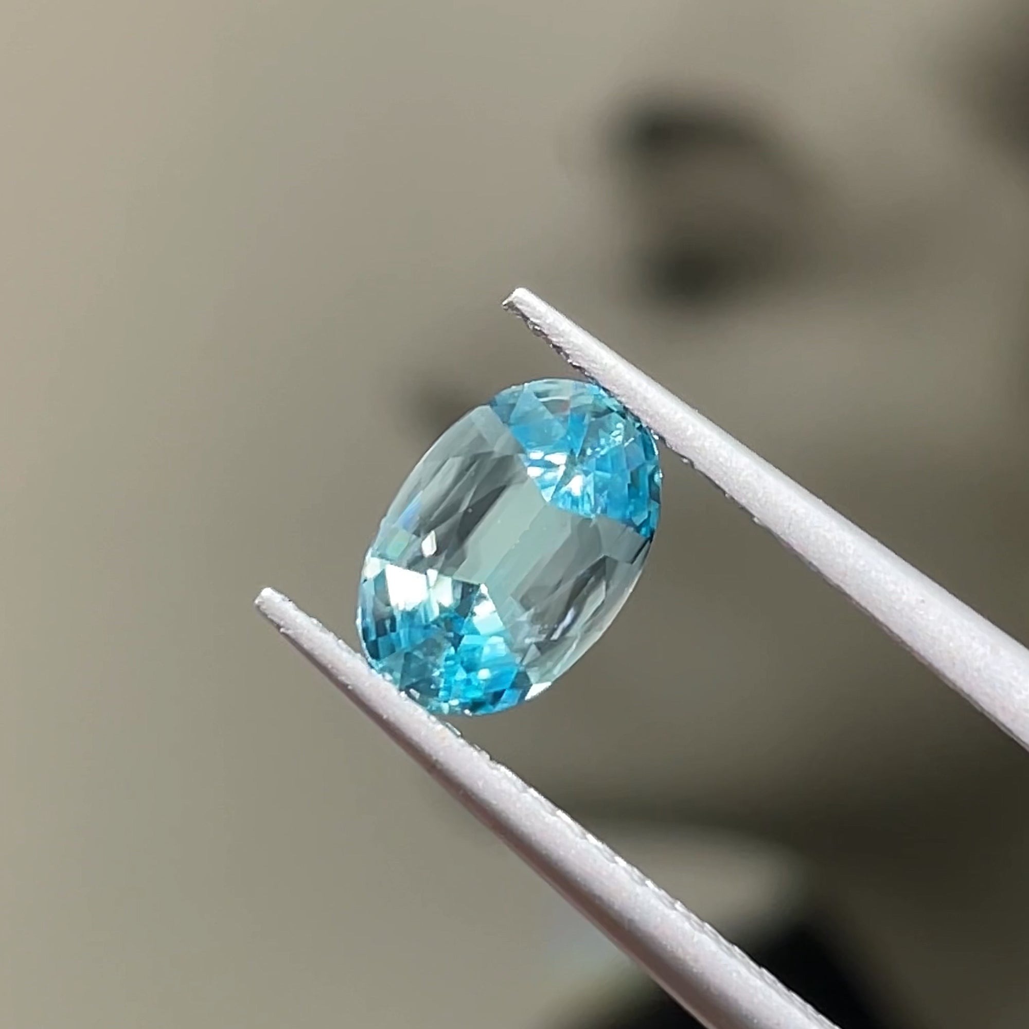 1.71 ct Cambodian Blue Zircon, precision cut oval, tweezers view, grey background